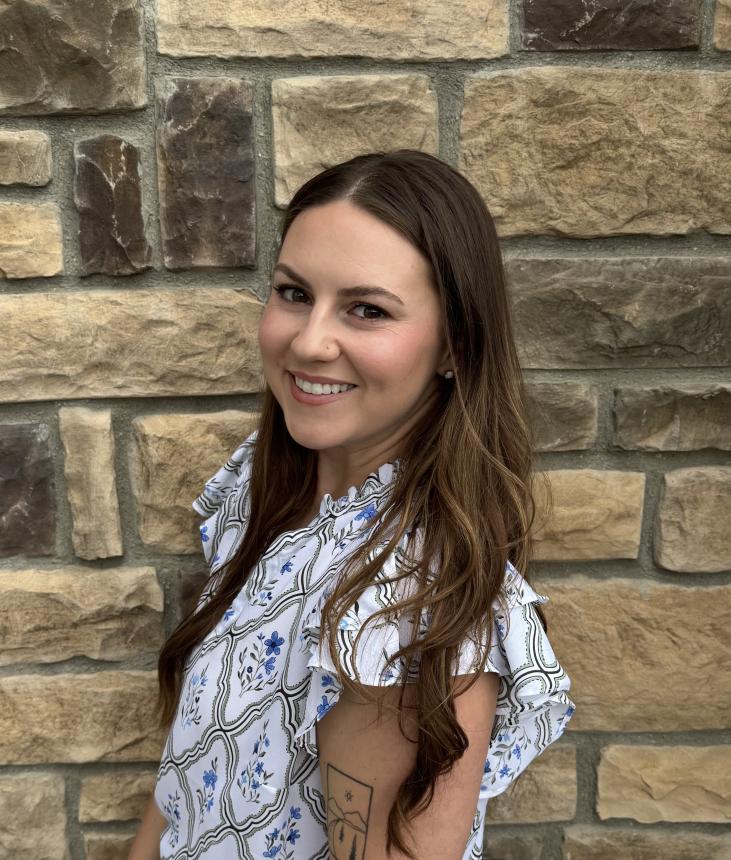 white young woman with dark hair standing in front of a brick wall. she is wearing a white shirt with blue floral designs.